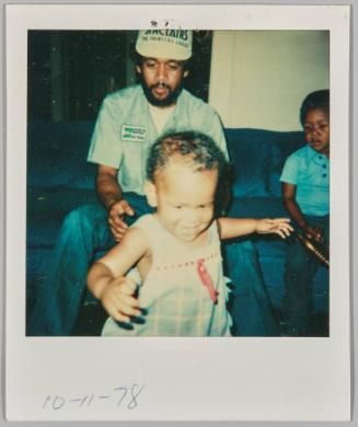 10-11-78 [Toddler walking, man in work uniform standing behind with arms out]