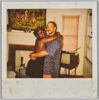[Young man and woman hugging in living room in front of television set]

