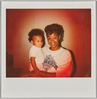 [Woman holding toddler in her arms, smiling and wearing a white graphic sweatshirt]


