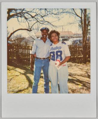 [Man and woman standing together outside in fenced area, woman wearing shirt with numberr "88" printed on the front]
