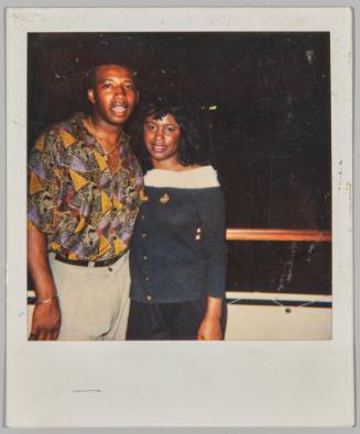 [Woman in white and black dress standing with man, man appears to be mid-speech]
