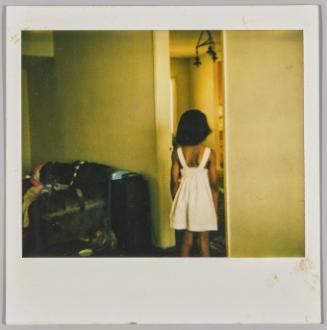 [Young girl standing in doorway with back turned, wearing white dress]
