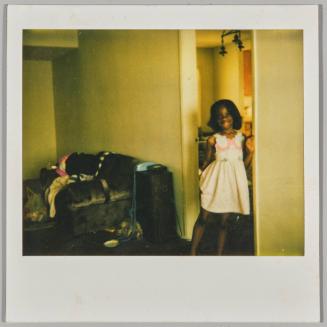 [Young girl standing in doorway smiling and leaning against door frame wearing white dress]
