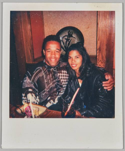 "George & [illeg.] at Benihana's May 16,1993 [Man in graphic sweater with his arm around woman in black jacket, they are sitting at table with drinks]