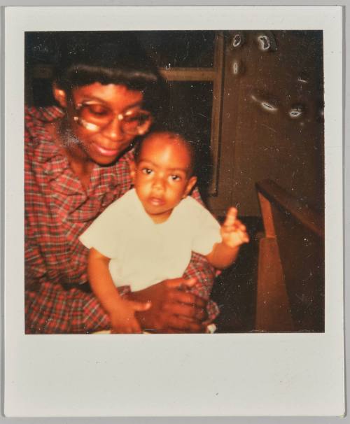 [Woman wearing glasses and plaid outfit holding baby, baby has one hand raised up]
