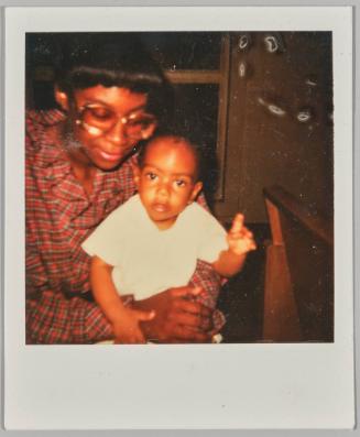 [Woman wearing glasses and plaid outfit holding baby, baby has one hand raised up]
