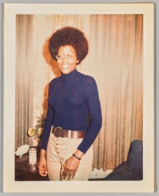[Portrait of woman smiling and wearing glasses in room with beige curtains, table behind her has a can on top]
