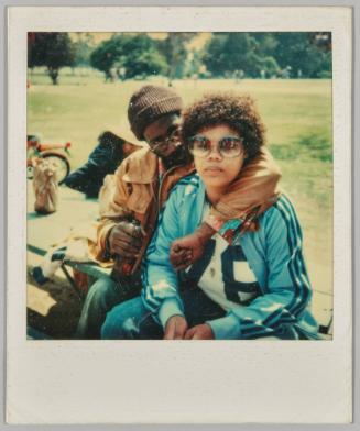 [Young man with arm around young women, both sitting on picnic table]
