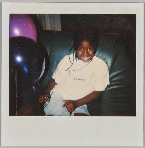 [Little girl smiling and sitting on black couch with purple and black balloons]
