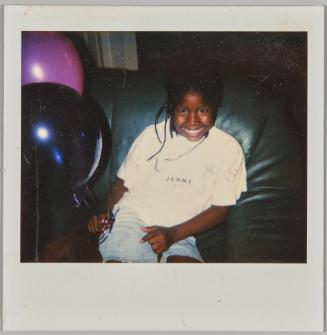[Little girl smiling and sitting on black couch with purple and black balloons]
