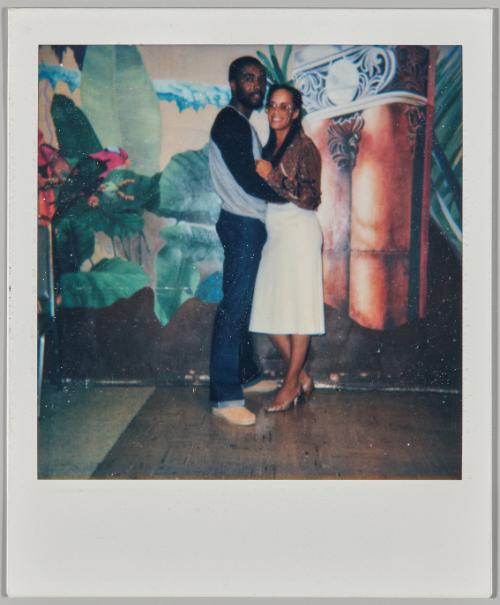 [Man and woman holding each other and standing in front of painted mural on back wall]
