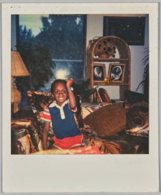 [Child smiling with arm raised in the air in a fist, appears to be evening from window in background]
