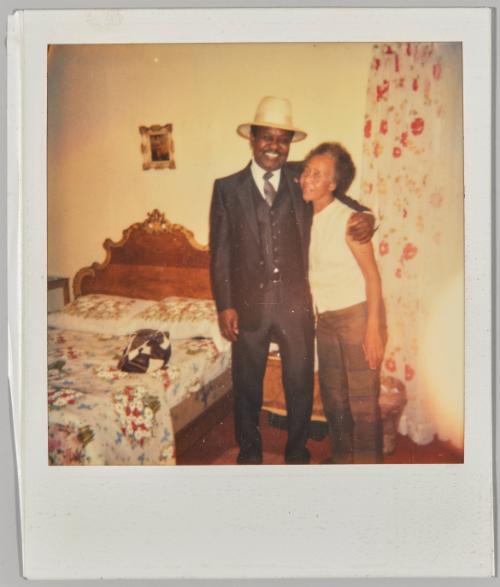 [Man in black suit and white hat smiling with arm around older woman]
