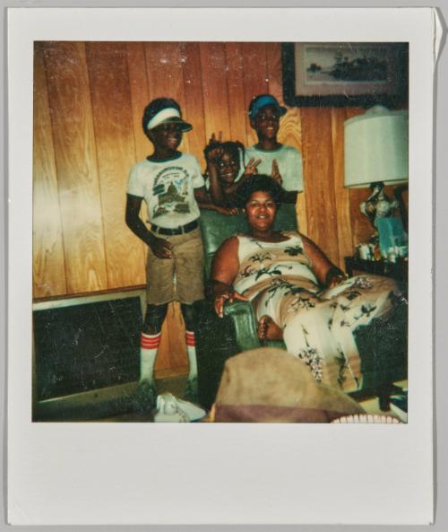 [Woman sitting in armchair, three children pose behind her]

