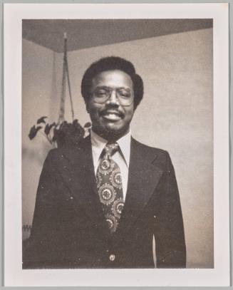 [Man with glasses and patterned tie standing in front of hanging plant]
