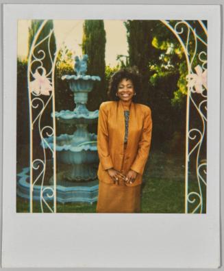 [Women in brown pencil skirt and blazer posing under white garden arch]
