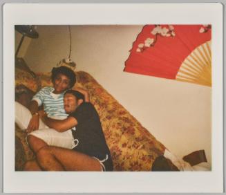 [Man cuddling with woman on couch, man appears to be sleeping as woman smiles, Japanese fan on wall]
