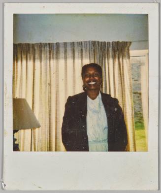 [Woman smiling in front of large window with curtain drawn, lamp in left corner]
