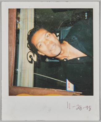 11-28-98 [Man with head cocked slightly to the right smiling in front of door with a number 2 painted on window]
