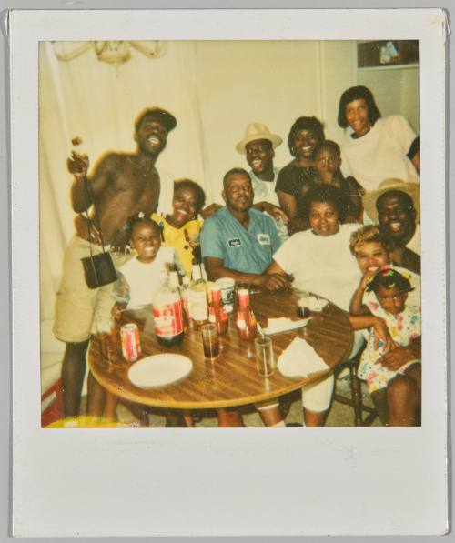 [Large gathering of adults and children grouped together around circle table in home]
