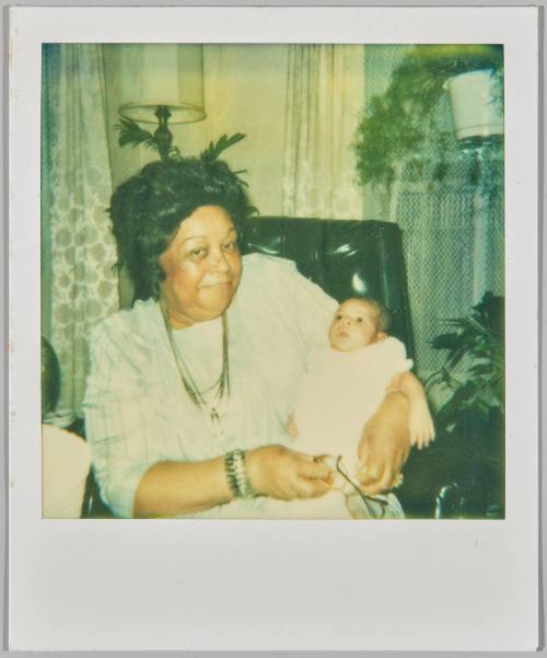 [Older woman holding baby in arms with reading glasses in hand]
