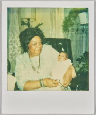 [Older woman holding baby in arms with reading glasses in hand]
