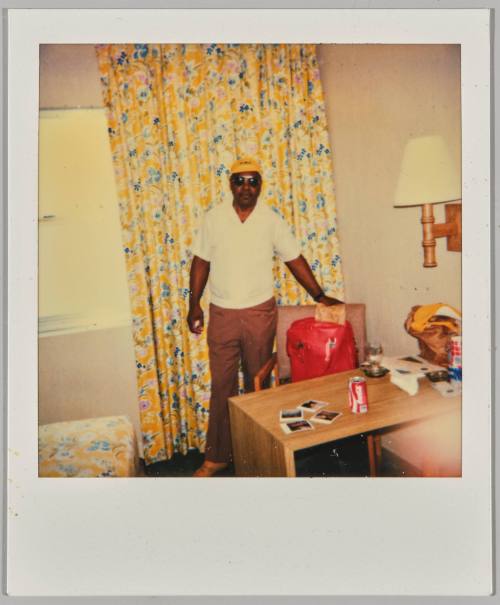 [Man with yellow hat standing in front of yellow floral curtain]
