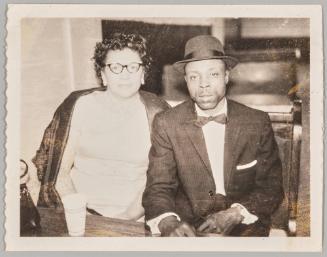 [Woman with cat-eye glasses sitting next to man in suit and bow tie]
