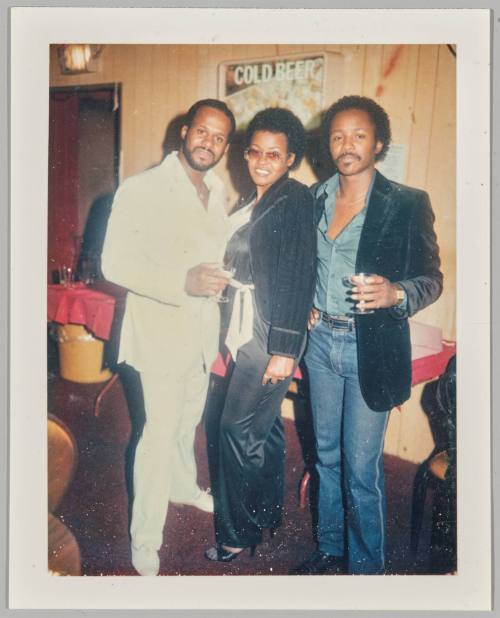 [Group of three posing, man on left in all white outfit]
