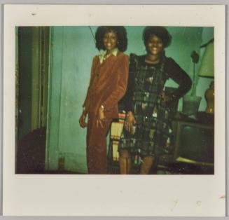 [Two women posing together in front of bookcase and television set]
