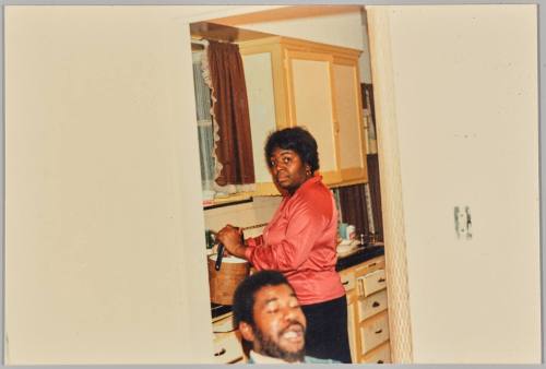 [Woman holding pot in kitchen doorway looking at the camera]
