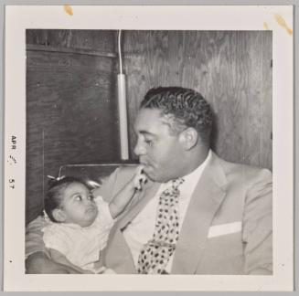 [Man holding baby in arms, baby placing two fingers on his lips]
