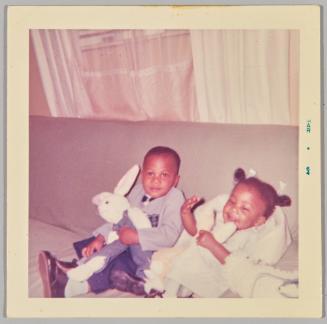 [Toddler boy and girl sitting on couch holding plush rabbits]
