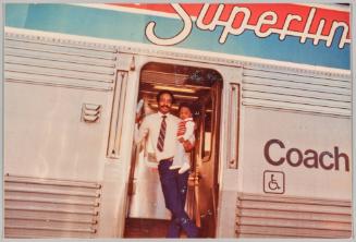 [Man holding toddler in doorway to train, train reads “COACH”]

