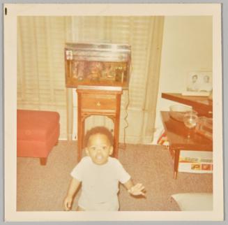 1970 [Toddler standing in living room, fish tank in the background]
