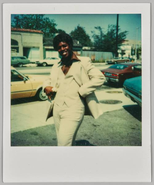 [Man smiling with hands on hips wearing white suit on street]
