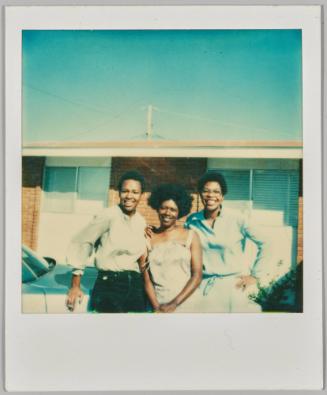 [Three women in blouses smiling and leaning on car in front of building]
