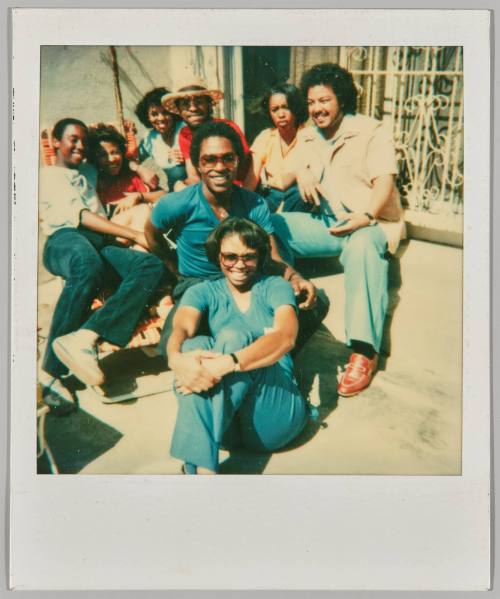 [Group of 8 young adults sitting in the sun smiling]
