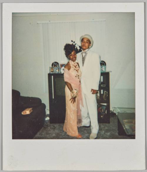 [Couple posing in home, woman wears formal pink dress and man wears white suit]
