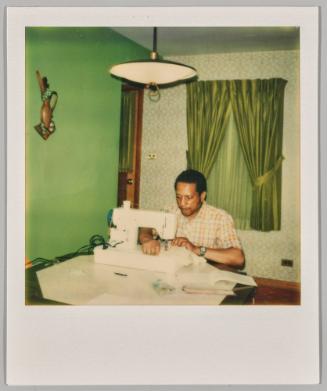 [Man sitting at table using a sewing machine]
