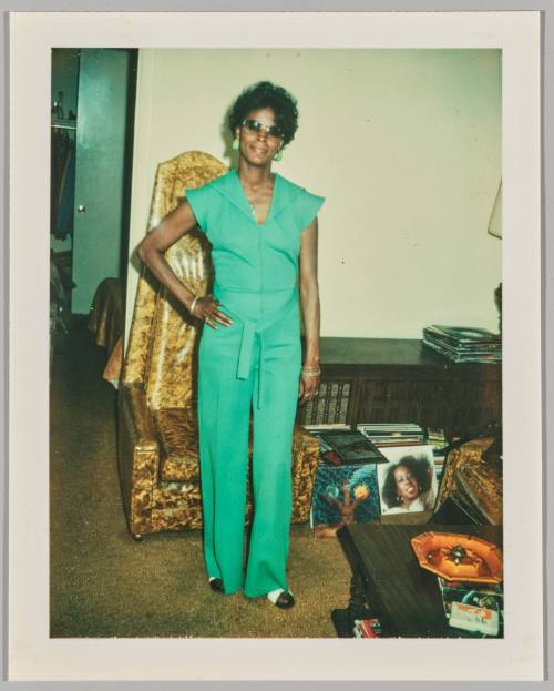 [Woman in green earrings and jumpsuit posing with hand on hip]
