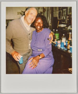 [Man holding a cigar with arm around woman wearing purple]
