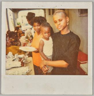 [Woman holding toddler in arms at barbeque]
