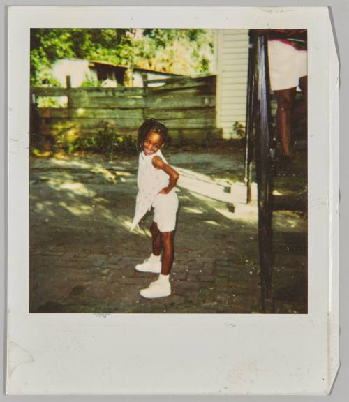 [Girl posing with hands on hips outside near wooden fence]
