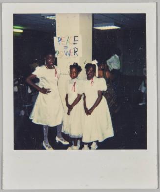 [Three girls in white dresses standing in front of "Peace is Power" sign]
