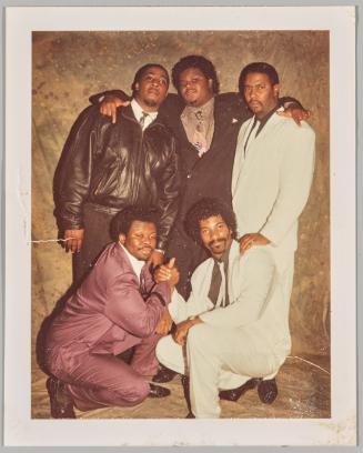 [Five men in suits posing in front of paint splattered backdrop]
