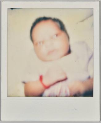 [Close-up of baby laying down with red wristband]
