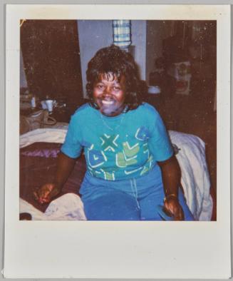 [Woman in turquoise graphic t shirt sitting on bed and smiling]
