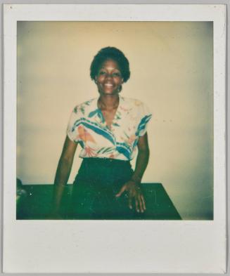 [Woman in patterned blouse smiling and sitting with hand on knee]
