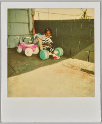 [Toddler smiling sitting on tricycle outside]
